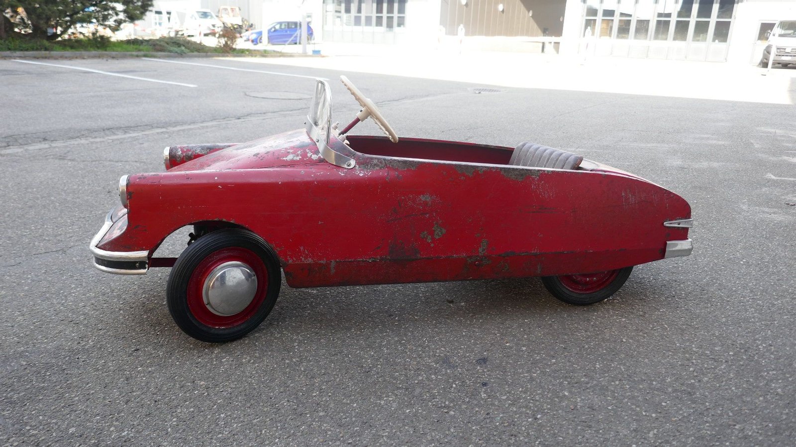 Am Straßenrand parkt ein rotes Tretauto.